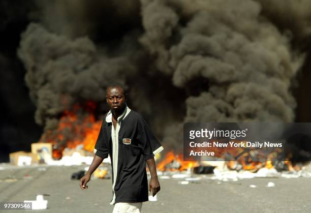 Dark clouds of smoke rise from a fire as a man walks through a Port-au-Prince street, where looting and violence were prevalent. Meanwhile, President...