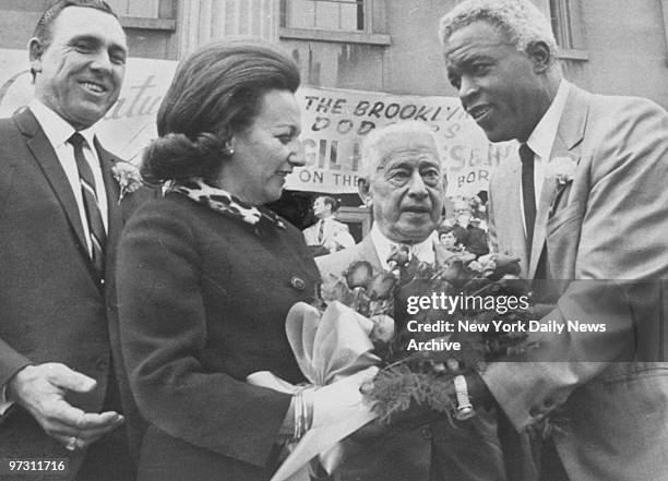 Gil Hodges looks on as his wife accepts flowers from Jackie Robinson.