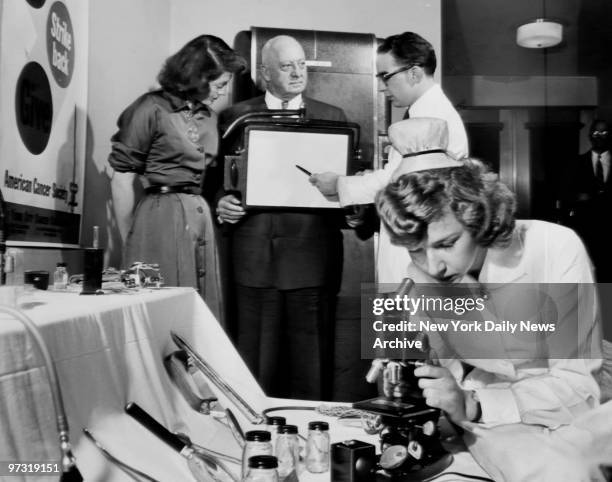 Nurse Vera Jacknitisky examines a specimen through a microscope as Dr. Alexander Vongries explains the operation of cancer-detection equipment to...