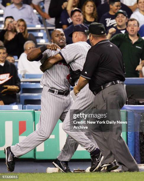 Minnesota Twins' bench coach Steve Liddle restrains the Twins' Torii Hunter as he and third base umpire Wally Bell get in between Hunter and home...