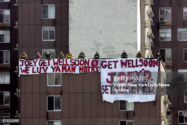 Members of two volunteer fire companies unfurl huge banners on a rooftop on Roosevelt Island to express get-well wishes for Firefighter Joseph...