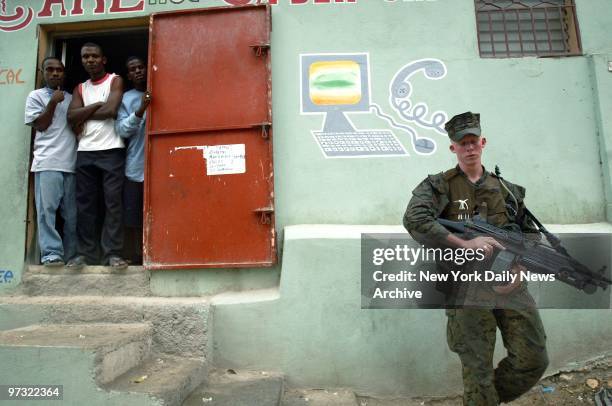 Group of men in a doorway look out as a Marine from the Lima Company, 3rd Battalion, 8th Marines patrols the streets of Port-au-Prince, Haiti. The...