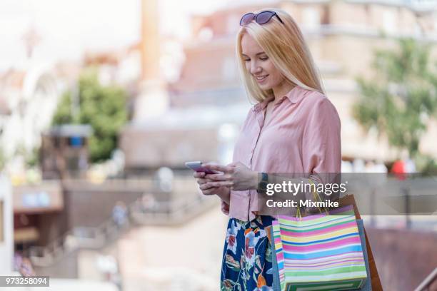 jeune femme avec shopping sacs en main envoyer des sms sur le téléphone - sms'en photos et images de collection