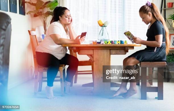 mother and daughter at home busy reading. - polynesian stock pictures, royalty-free photos & images