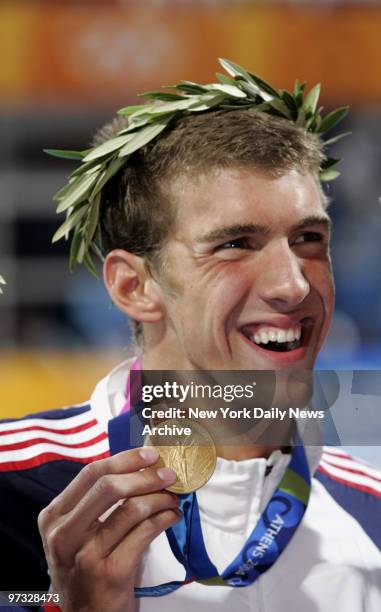 Swimmer Michael Phelps shows off his gold medal after coming in first in the 100-meter butterfly final at the Aquatic Center during the 2004 Summer...