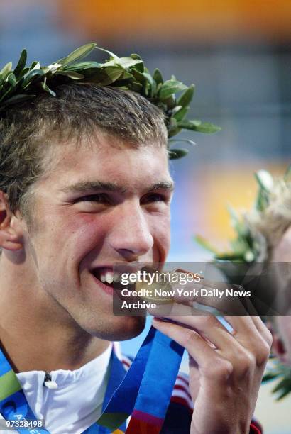 Swimmer Michael Phelps of the United States, bites his gold medal playfully after taking the top prize in the 400-meter individual medley at the...