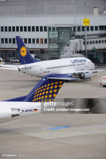 Tail-fin of Contact Air Interregional Fokker 100 taxiing and Lufthansa Boeing 737 parked at the terminal behind.