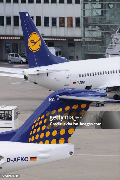 Tail-fins of Contact Air Interregional Fokker 100 taxiing and Lufthansa Boeing 737 parked at the terminal behind.