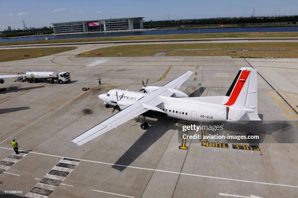 Marshaller with bats controlling CityJet Fokker F-50 taxiing at London City with refuelling bowser behind