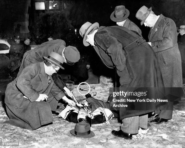 Detectives examine the body of gangster Louis Cohen, the killer of Kid Dropper, after he was shot to death on Lewis St. Cohen's gun lies near his...