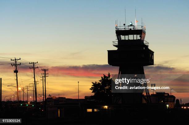 Air traffic control-tower at dusk with lights on, green rotating-beacon and telegraph poles.