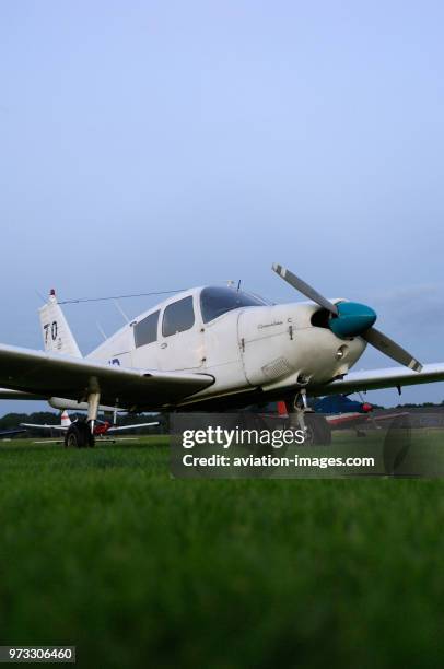 A Piper PA-28-180 Cherokee parked on the grass at dusk.