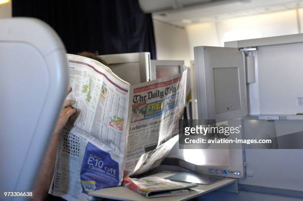 Passenger reading The Daily Telegraph newspaper sitting in the Club World business-class cabin seats of British Airways Boeing 747-400 enroute...