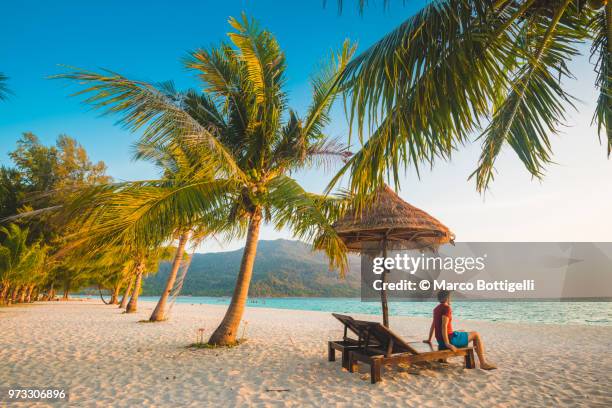 tourist admiring the sunrise from a deckchair on tropical beach, thailand - wonderlust stockfoto's en -beelden