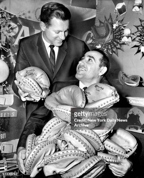 Yankee Yogi Berra is up to his ears in catchers mitts, thanks to his summer pal, Whitey Ford. Scene was a Sporting Goods Fair at midtown hotel.
