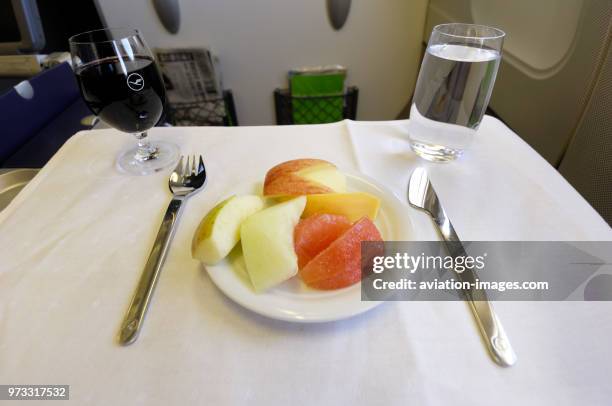 Fresh fruit meal with metal knife and fork cutlery, with glasses of red wine and water drinks in the business-class cabin in the Lufthansa Airbus...
