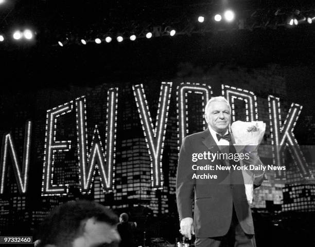 Ol' Blue Eyes Frank Sinatra clutches bouquet of flowers handed to him by an admirer following show at Radio City Music Hall.