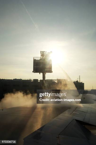 Man standing on a cherry picker platform, spraying de-icing fluid on an aircraft wing in the early morning before the airliner can take off. Winter..