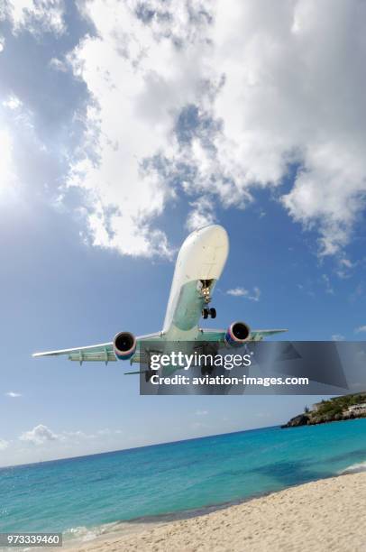 Very low on final-approach to landing over Maho Beach with cumulus clouds behind.