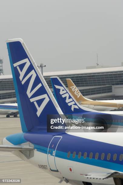 Tail-fins of an ANA All Nippon Airways Airbus A320-200, Boeing 737 and an ANK 737 parked at the terminal and taxiing behind.