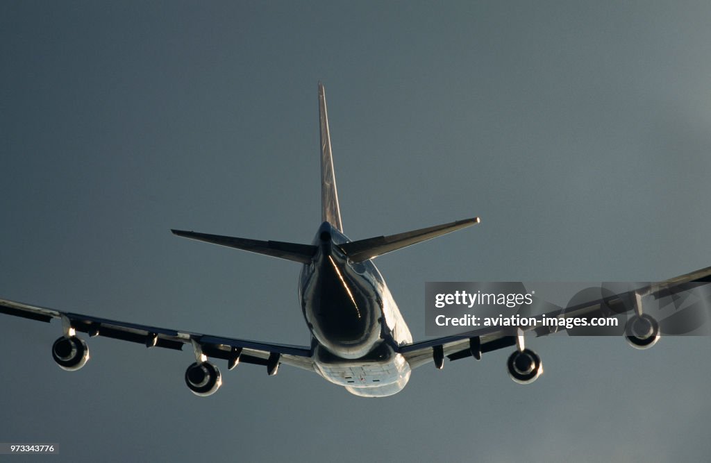 British Airways Boeing 747-100 climbing enroute on a grey-cloudy-day with sun glinting off the fuselage and wings