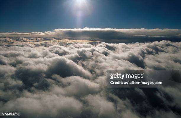 A layer of alto-cumulus clouds in the forground and a cumulo-nimbus cloud and the sun behind at high-altitude.