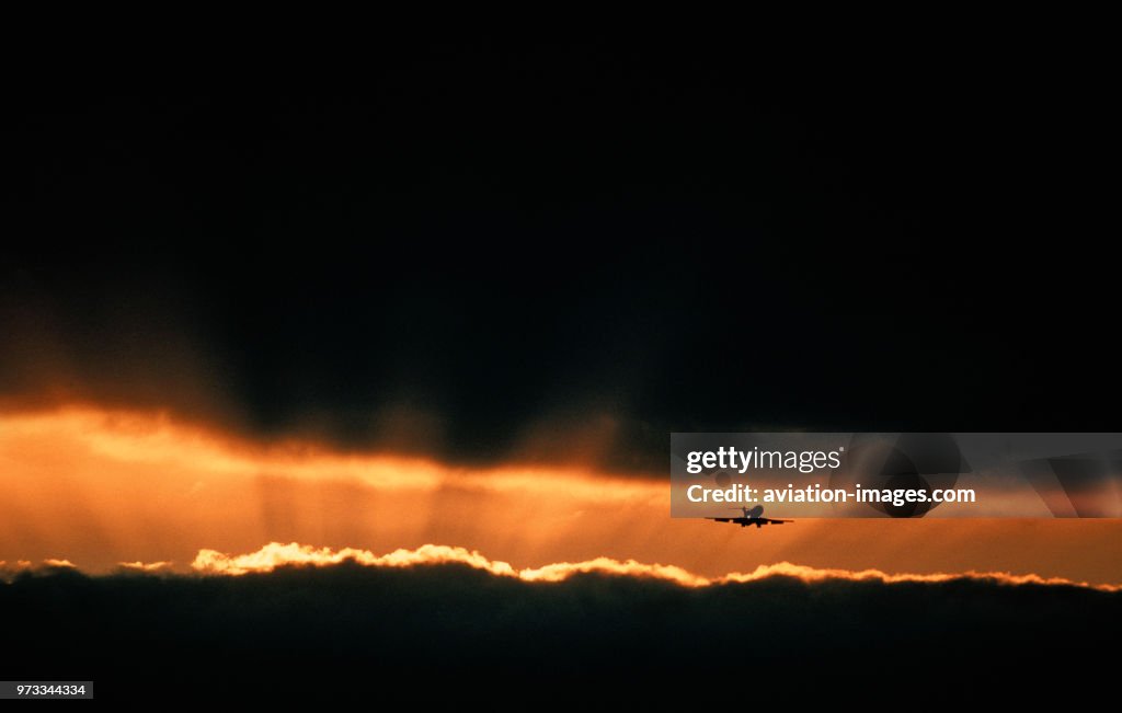 Boeing 727 final-approach at sunset with sunburst shafts of sunlight radiating outwards from behind dark clouds with silver-linings