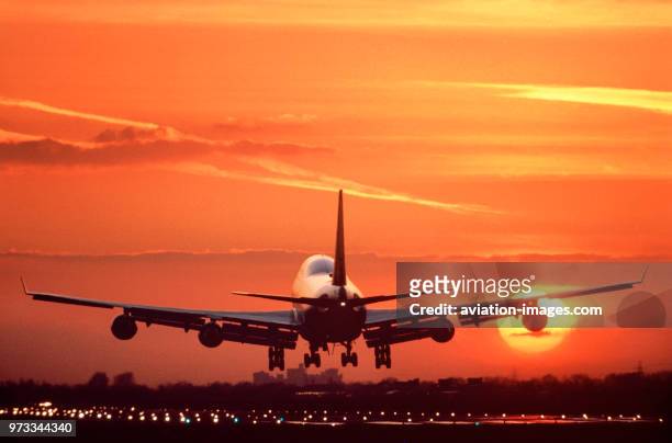 Boeing 747 landing on the runway at sunset with runway-lights on and Windsor Castle in the distance behind.