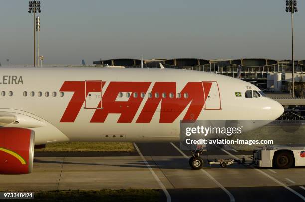 Towed by a tug along a taxiway and crossing an airside vehicle road with a big TAM logo on the fuselage.