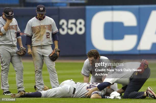 Washington Nationals' Jose Vidro and Felipe Lopez look on as rightfielder Austin Kearns and a team trainer check out first baseman Nick Johnson after...