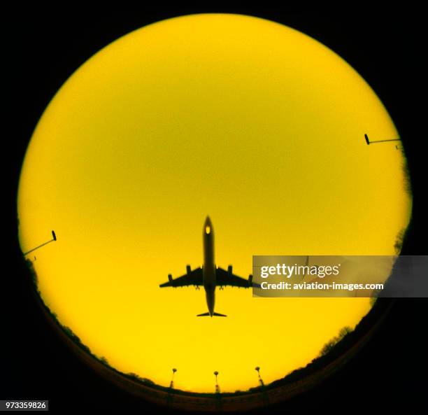 Circular colourised yellow sky with fisheye view of an Airbus A340 flying over approach-lights.