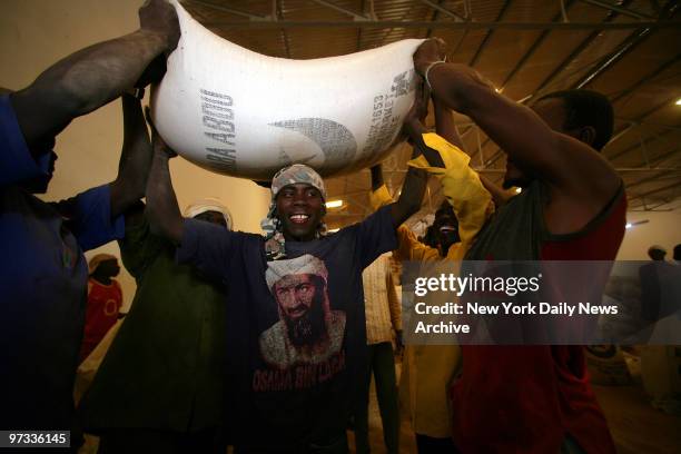 Wearing an Osama Bin Laden T-shirt and a smile, a worker at a World Food Programme warehouse has his colleagues place a large bag of millet onto his...