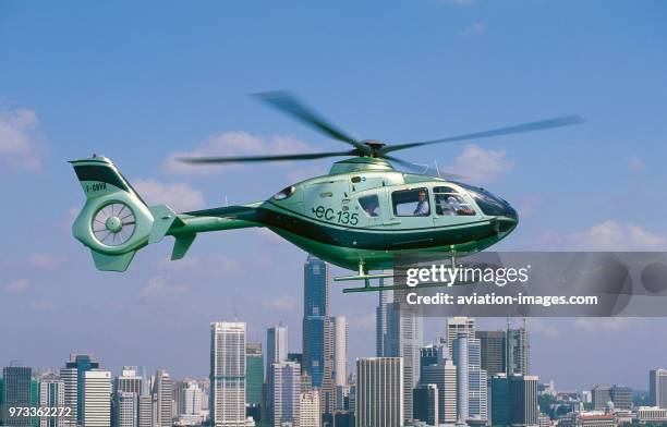 Eurocopter EC-135T1 flying enroute over the central business district of downtown Singapore with skyscrapers behind.