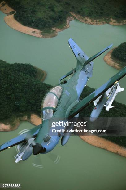 Brazilian Air Force Embraer EMB-314 Super Tucano banking over river and trees.