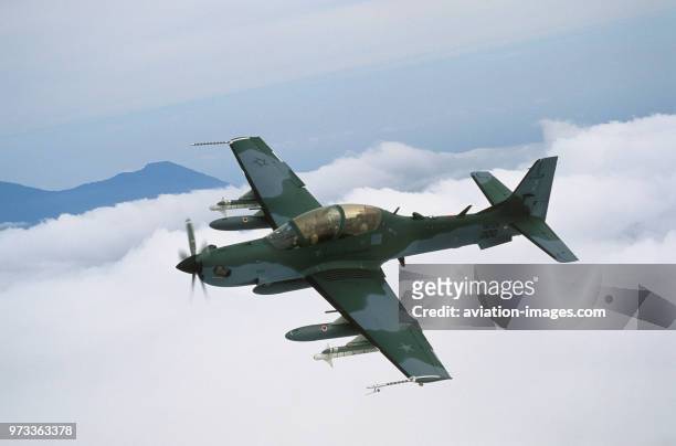 Brazilian Air Force Embraer EMB-314 Super Tucano banking over clouds and hills.