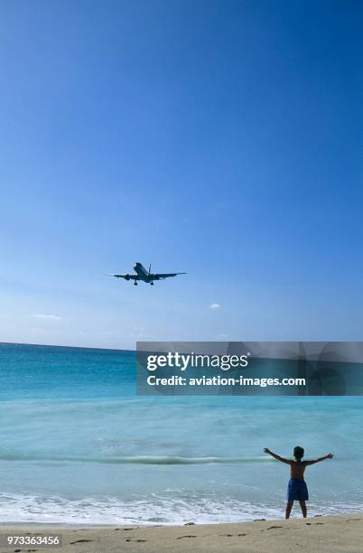 Airways Boeing 757-200 on very low final-approach landing over Maho Beach with boy child standing on beach waving.