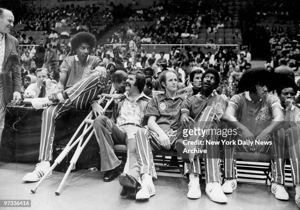 Wendell Ladner sits with his crutches on the sidelines with teammates, including Julius Erving, during a game against the Utah Stars at Nassau...