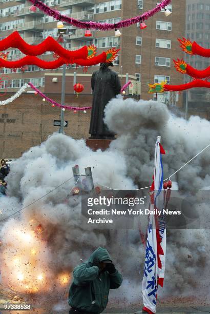Passerby covers his ears as firecrackers explode around statue of Commissioner Lin Ze Xu during Chinese New Year festivities at Chatham Square on...