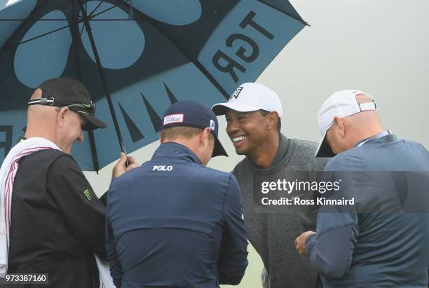 Tiger Woods of the United States talks with Justin Thomas of the United States and caddie Joe LaCava on the practice range during a practice round...