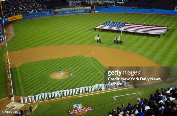 With a large American flag adorning centerfield, the players line up along the Yankee Stadium first base line in a pregame ceremony honoring the...