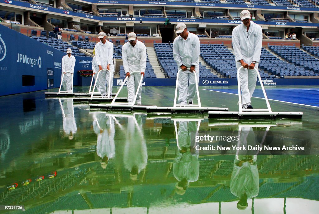 Workers sweep water off the court at Arthur Ashe Stadium dur