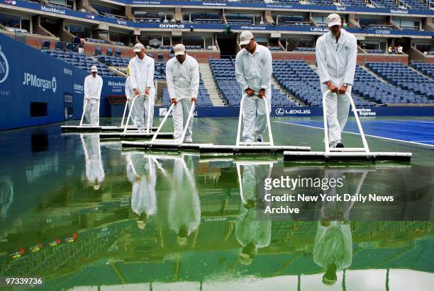 Workers sweep water off the court at Arthur Ashe Stadium during a rain delay at the U.S. Open in Flushing Meadows-Corona Park. Due to the heavy...