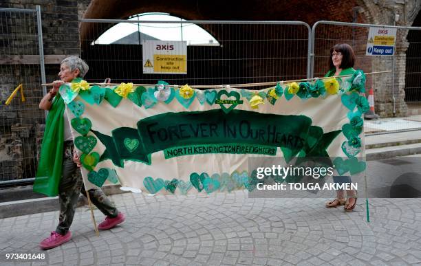 Women carry a banner painted with the Words Forever in our Hearts" and "Kensington Firefighters", near the Grenfell Tower in west London on June 13,...