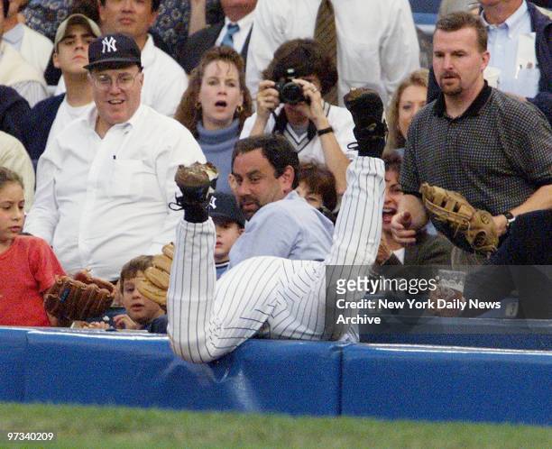 Yankees' first baseman Tino Martinez goes head first into the stands while chasing a foul ball in the first inning. Martinez and a gloved fan both...