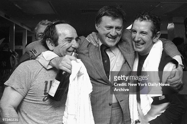 Yankees' owner George Steinbrenner hugs coach Yogi Berra and manager Billy Martin as they celebrate victory with champagne.