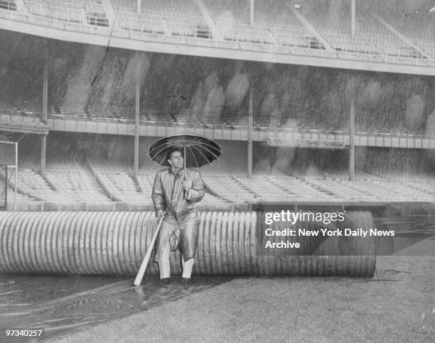 Yankees' shortstop Phil Rizzuto sits under umbrella in the rain at Yankee Stadium.