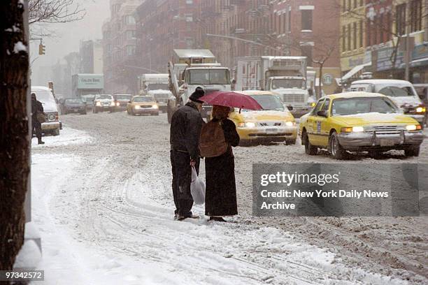 Pedestrians wait to cross Ninth Ave. Between W. 45th and 46th Sts., where early morning traffic has turned the snow into slush..