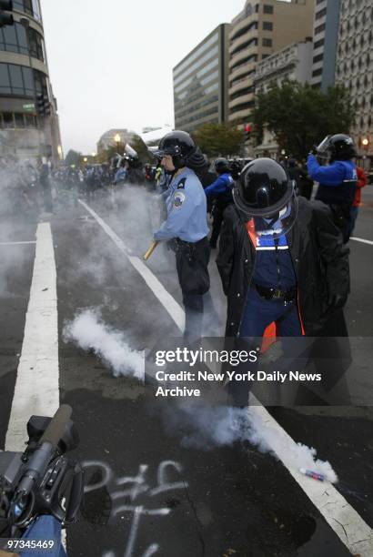 Police officer kicks aside a canister of tear gas as cops face off against demonstrators protesting the policies of the International Monetary Fund...