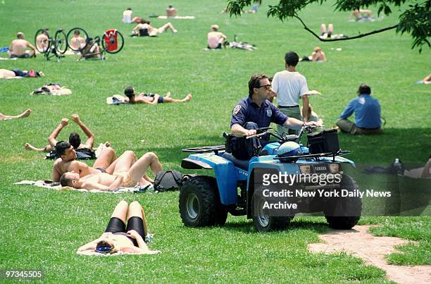 Police officer patrols the Sheep Meadow in Central Park as sunbathers take in the sun.