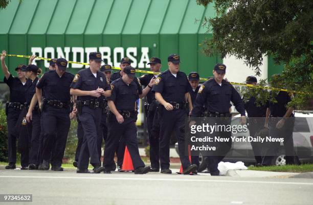 Police officers search the area in front of the Ponderosa steakhouse in Ashland, Va., where a man was shot Saturday night. Investigators, acting on...